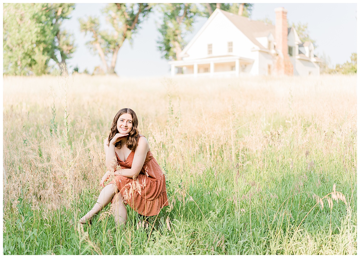 brown haired girl in orange dress sitting in field with white house