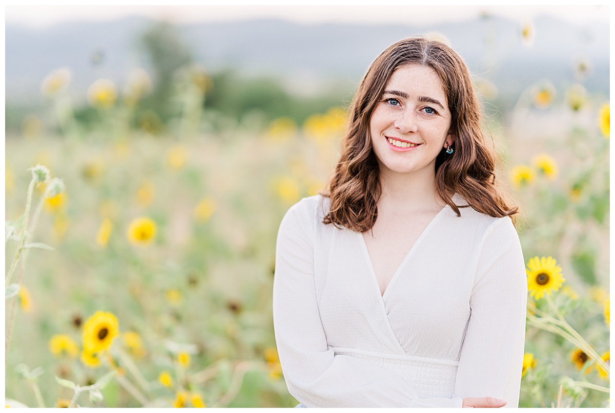 Brown haired girl smiling next to sunflowers