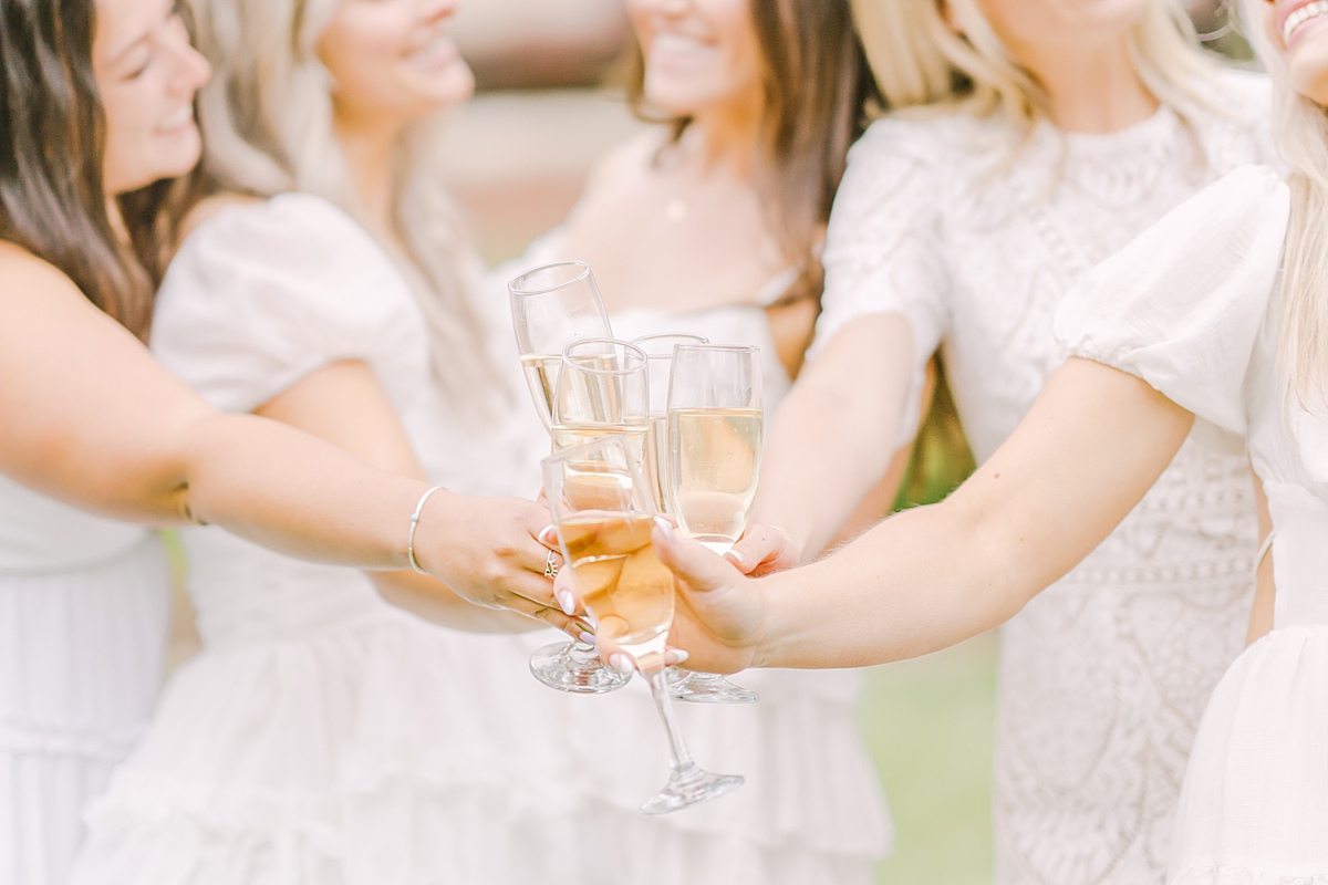 Five senior grads in white dresses clink champagne glasses.
