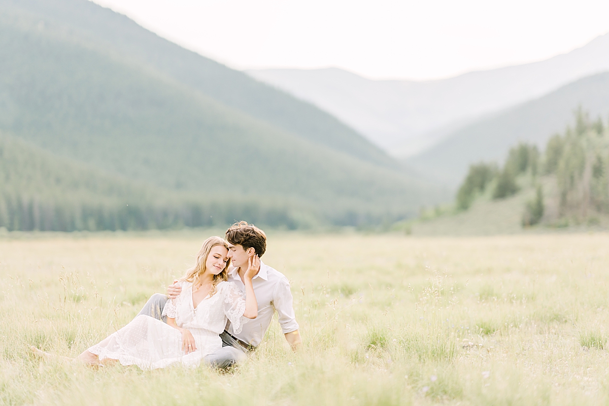 An engaged couple rests in a field.