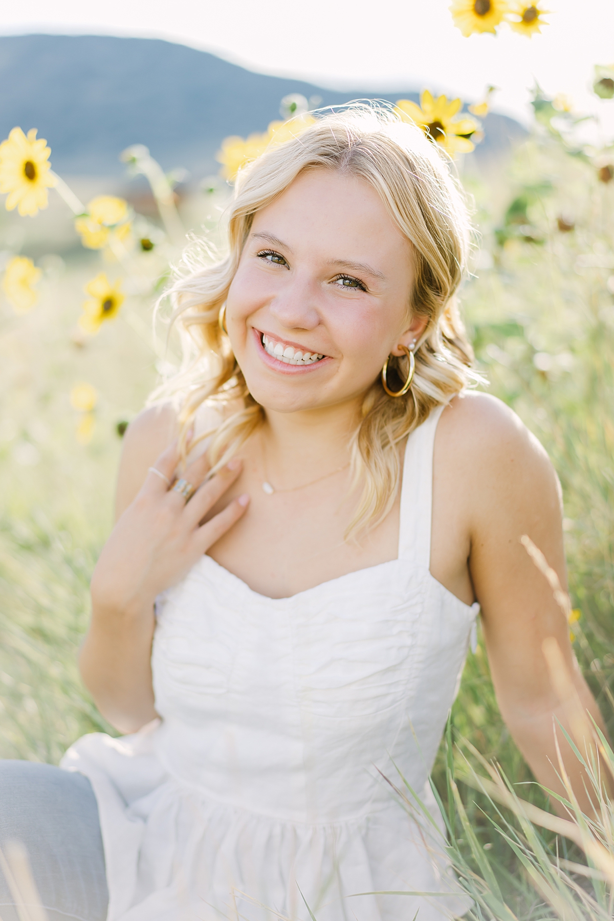 A cute 2023 Littleton senior smiles at the camera while sitting by the sunflowers.