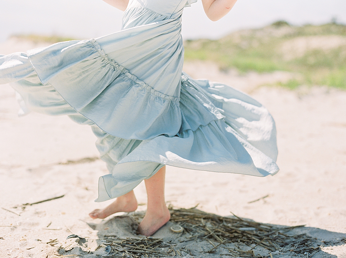A young girl twirls on the beach in a ruffled blue dress.