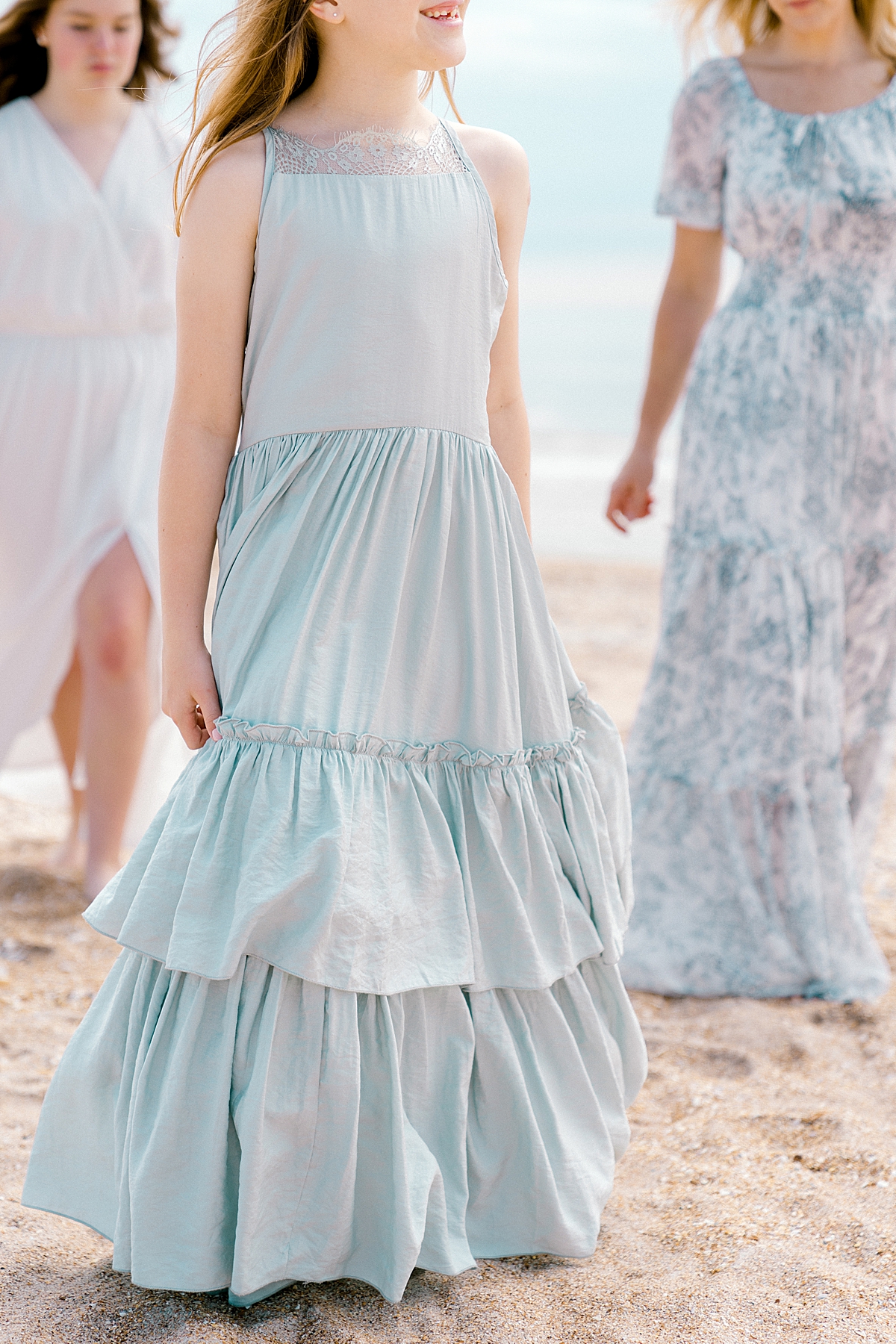 A young girl walks at the beach by the ocean in a pretty blue ruffled long dress.