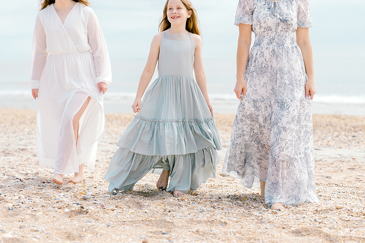 Three women walk along the beach in pretty dresses.
