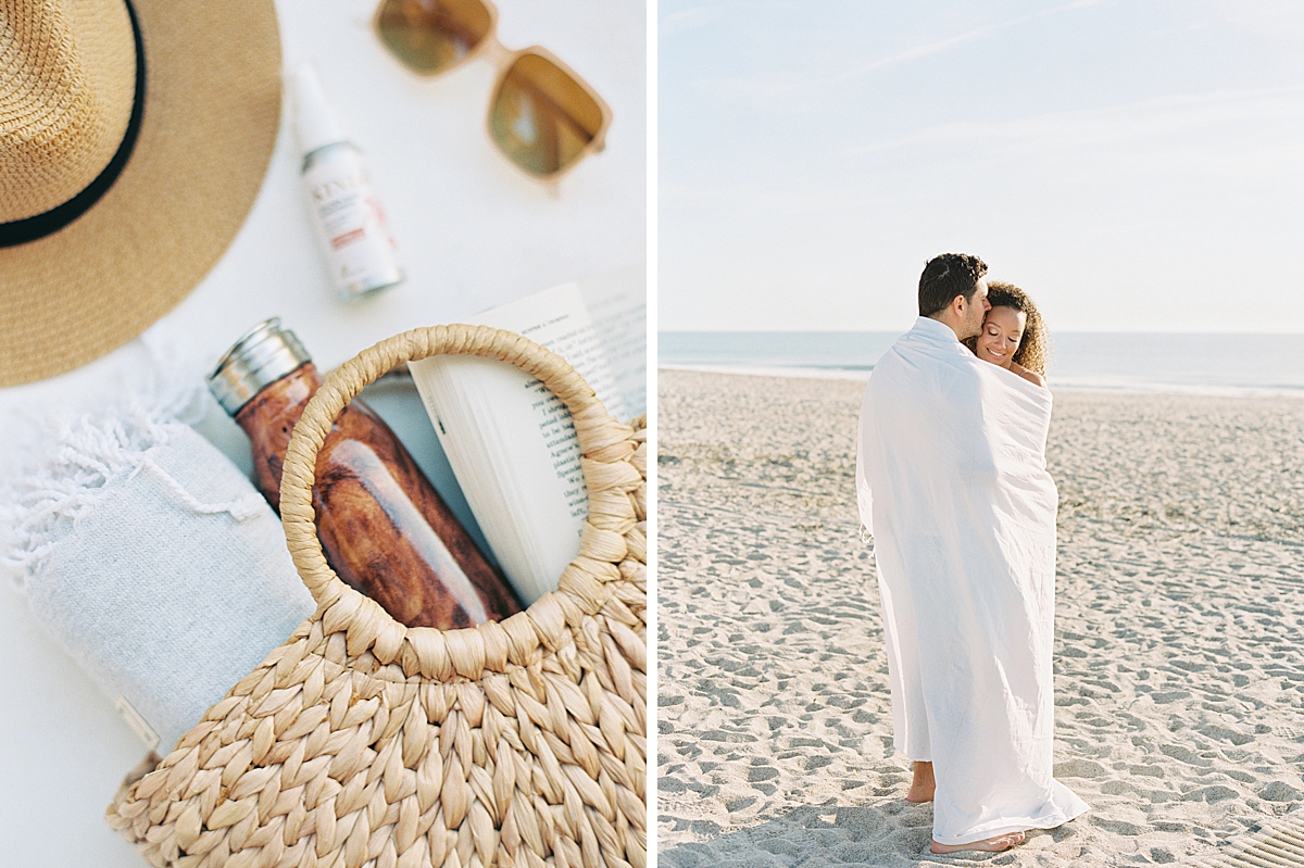 A romantic couple wraps up in a blanket at the beach.