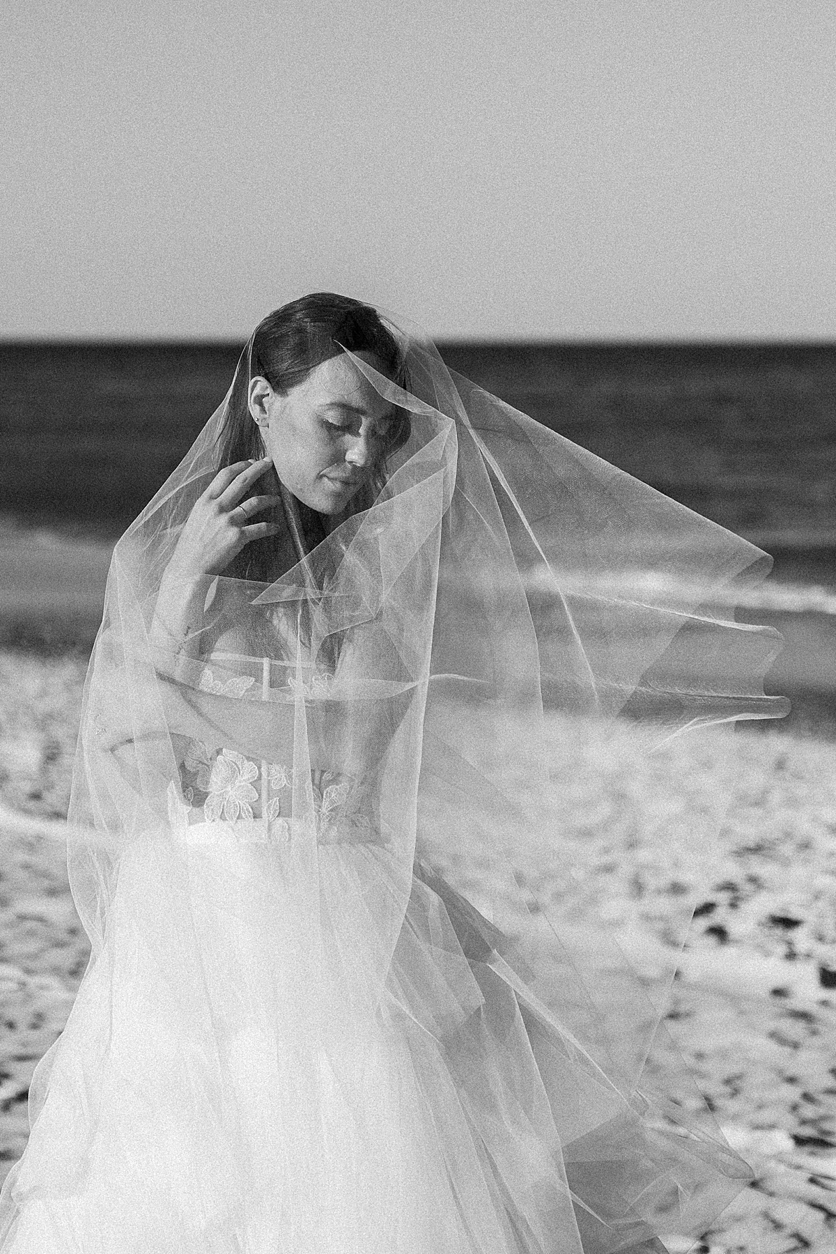 A bride stands by the ocean in a Madeleine Fig veil.