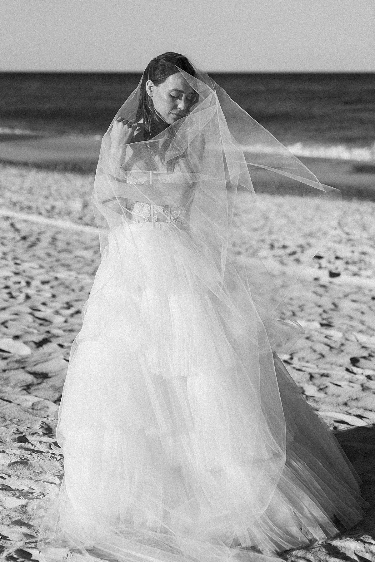 A bride stands on the beach in a Madeleine Fig veil and Elizabeth Leese wedding dress.