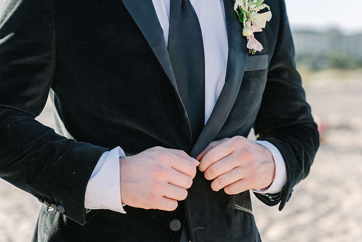 A groom in a black velvet suit buttons his jacket.