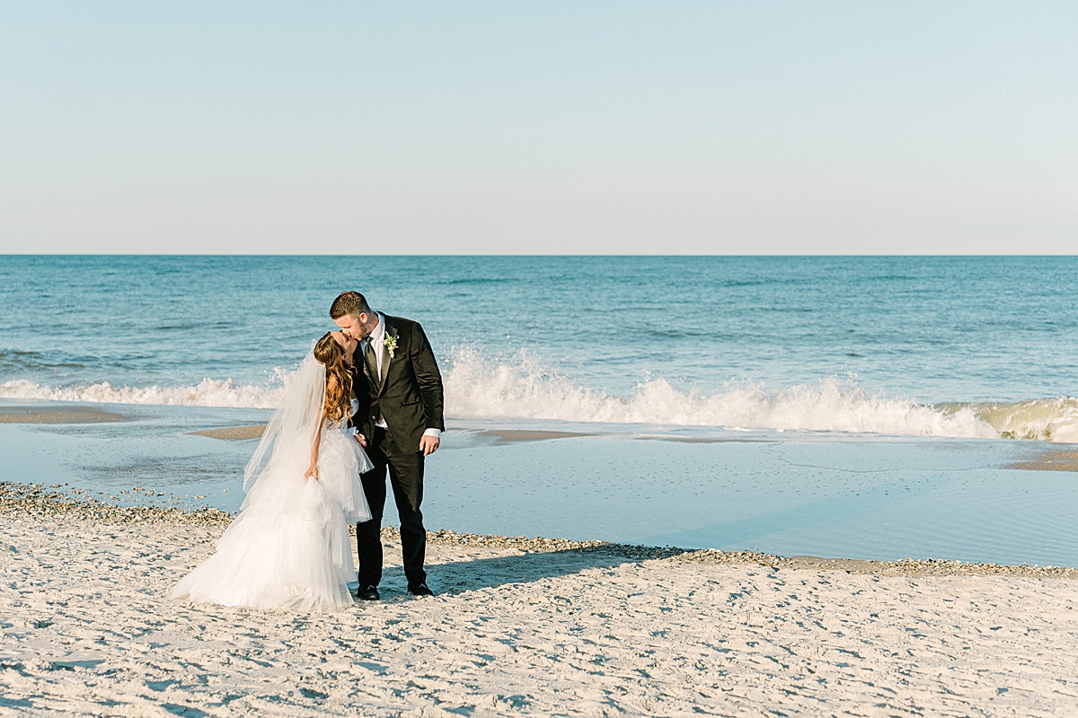A bride and groom kiss on the beach in Florida as the waves crash behind them.