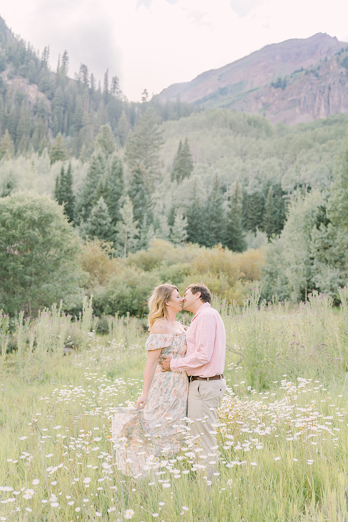A couple kisses in the wild daisies in Aspen Colorado during their engagement photos.