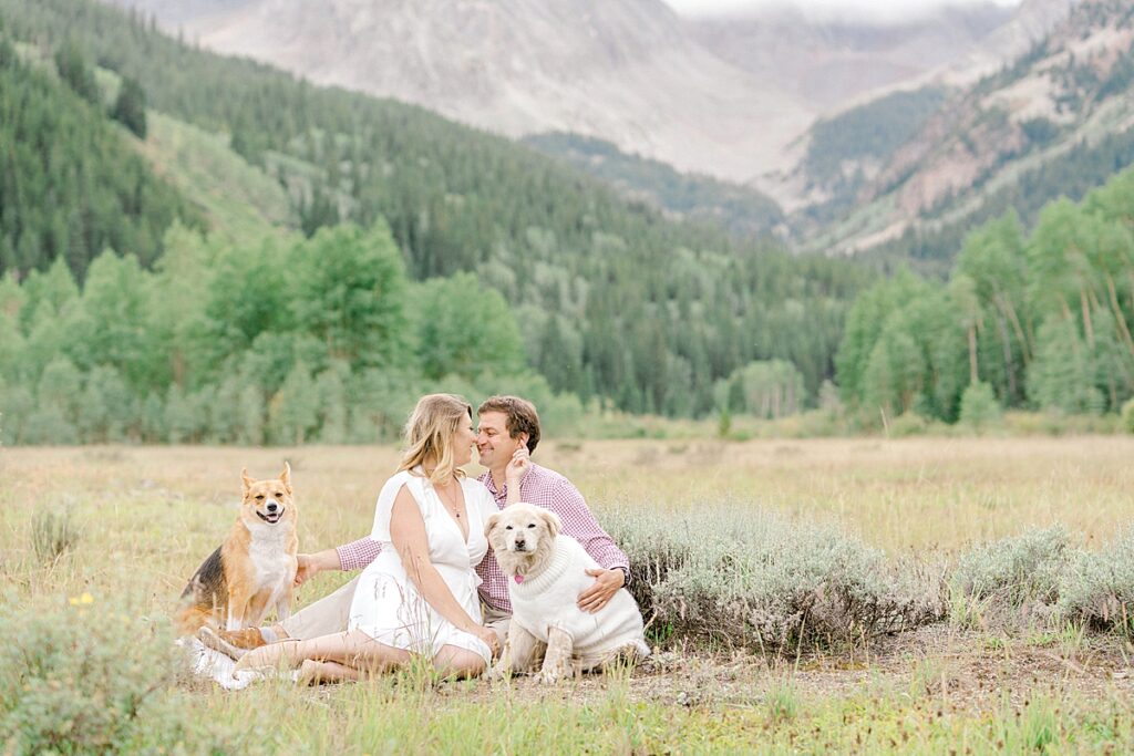 A couple embraces in a meadow sitting next to their dogs during their Aspen colorado engagement photos session.