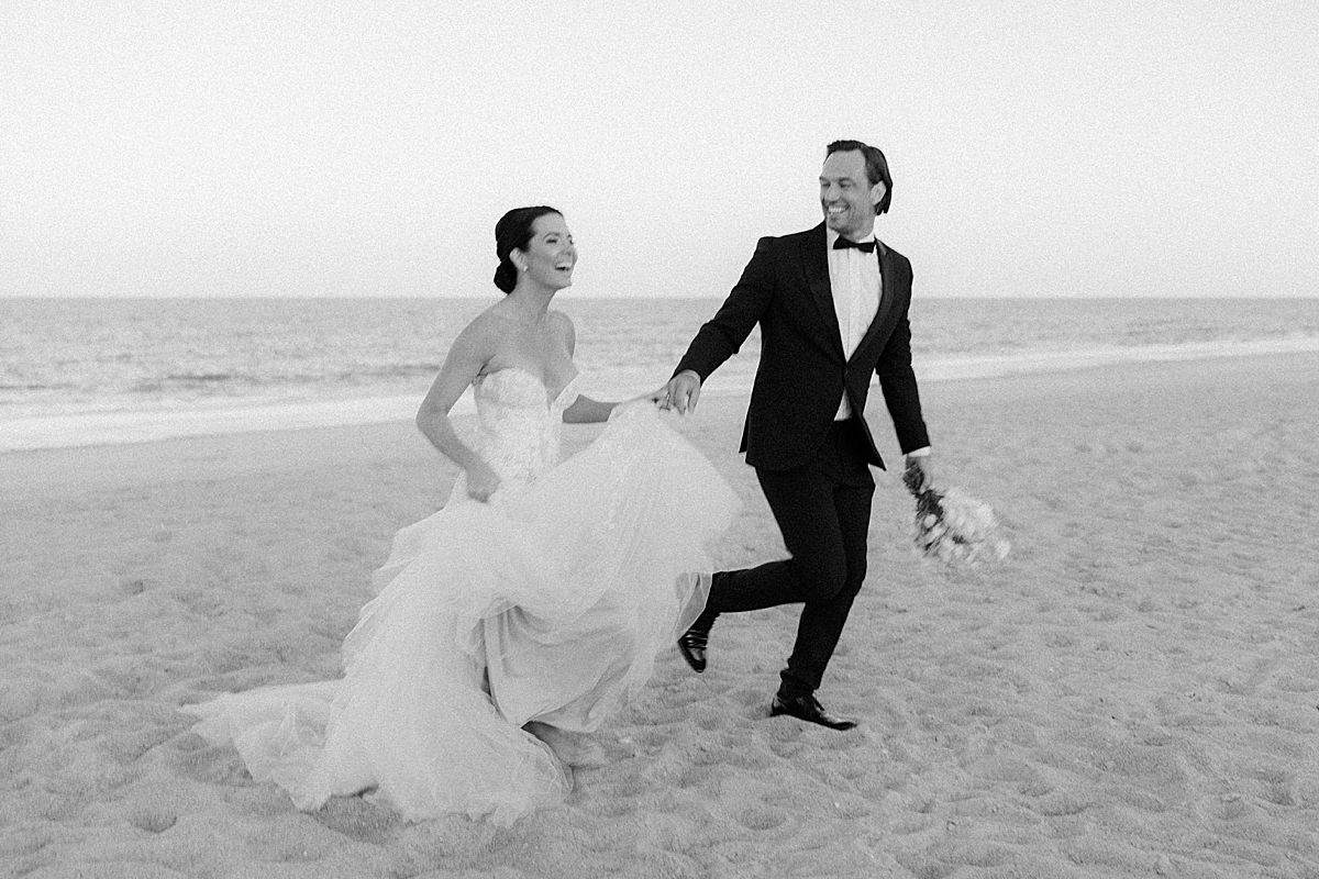 A gorgeous couple runs across the beach in their wedding attire at their luxury beach wedding on film.