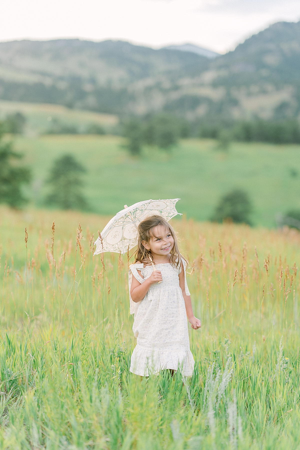 A cute little girl spins with a parasol in the mountains.