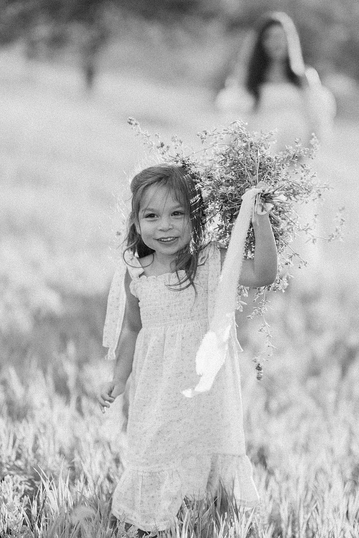 A cute 3 year old girl runs towards the camera with a bouquet in her hands.