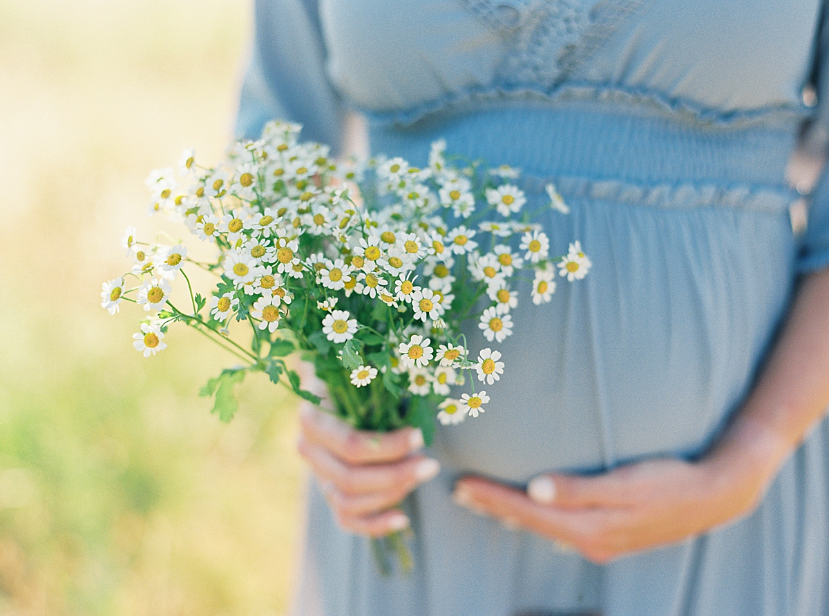 A pregnant woman in a blue dress holds a bouquet of chamomile.