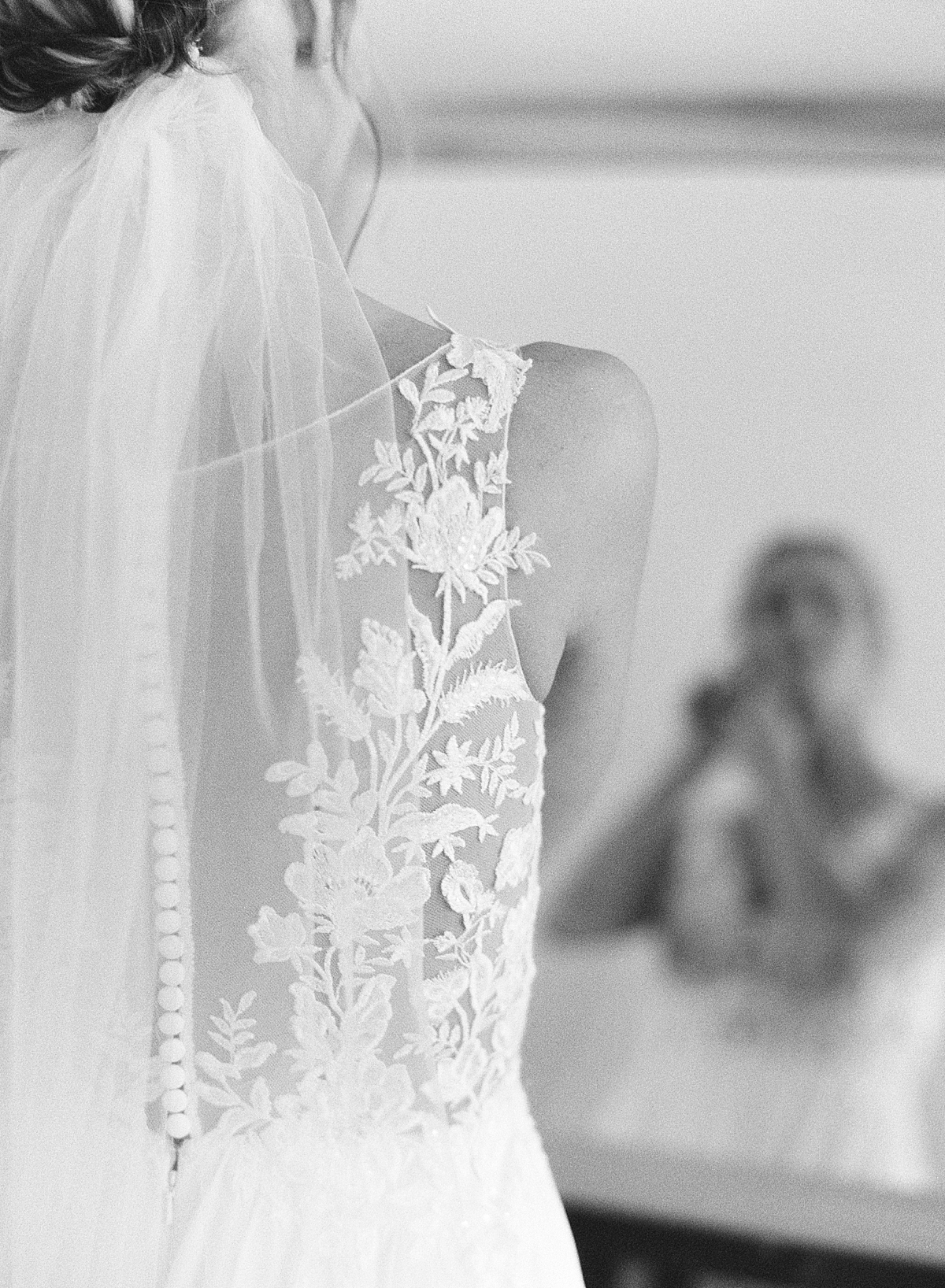 A bride puts on her earrings while looking into the mirror on black and white film.