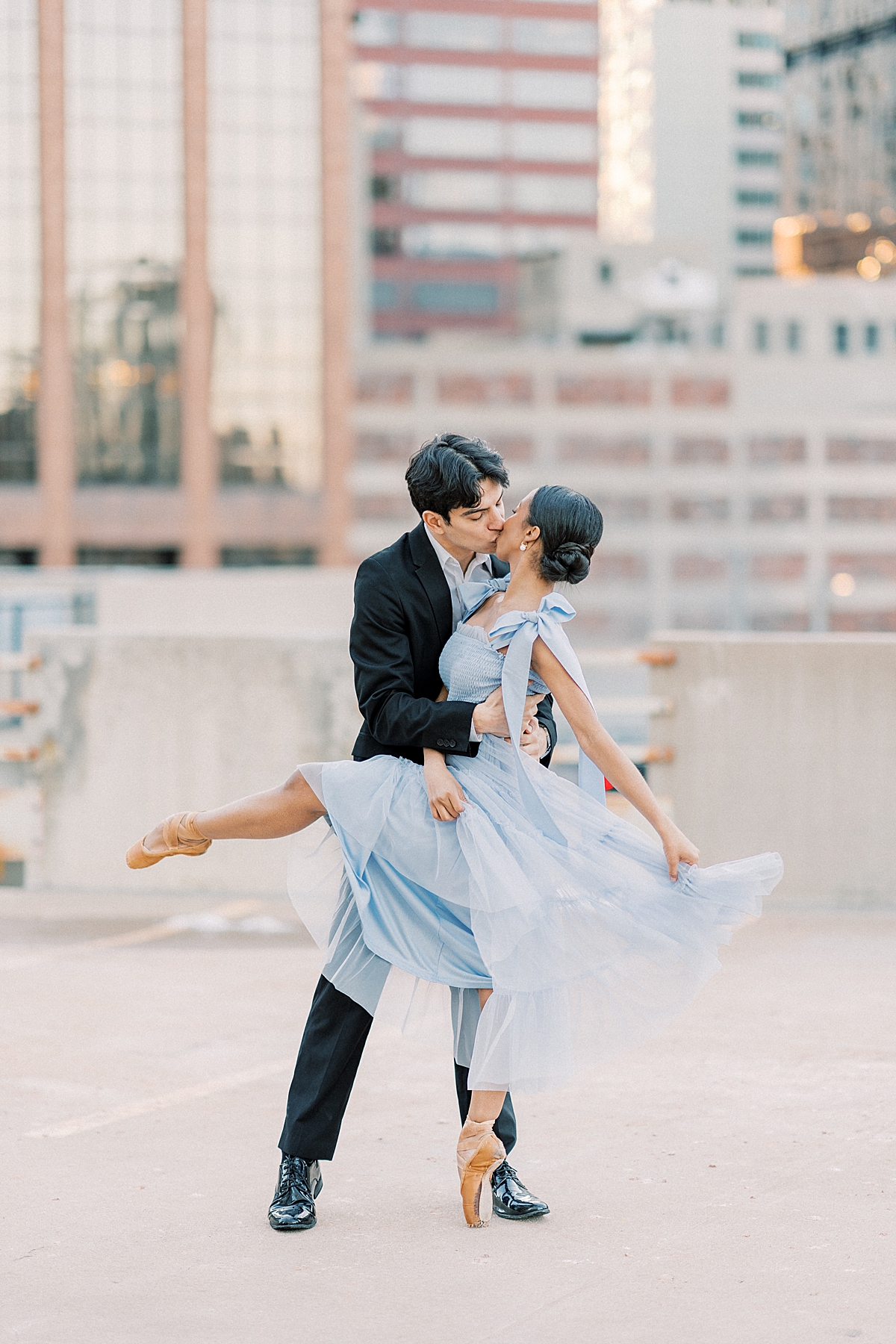 Two ballet dancers share a kiss with the Denver downtown skyline in the background.