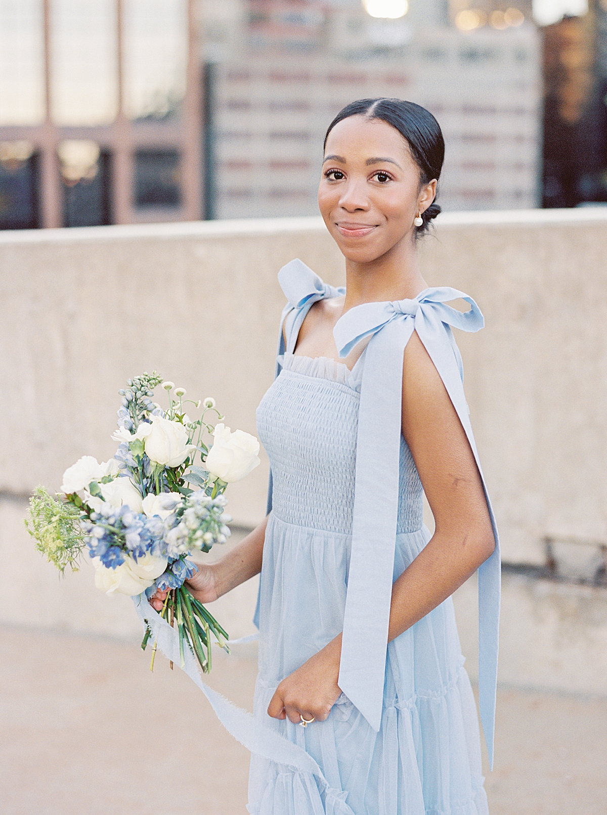 Sheridan holds a beautiful blue and white bouquet and smiles at the camera.