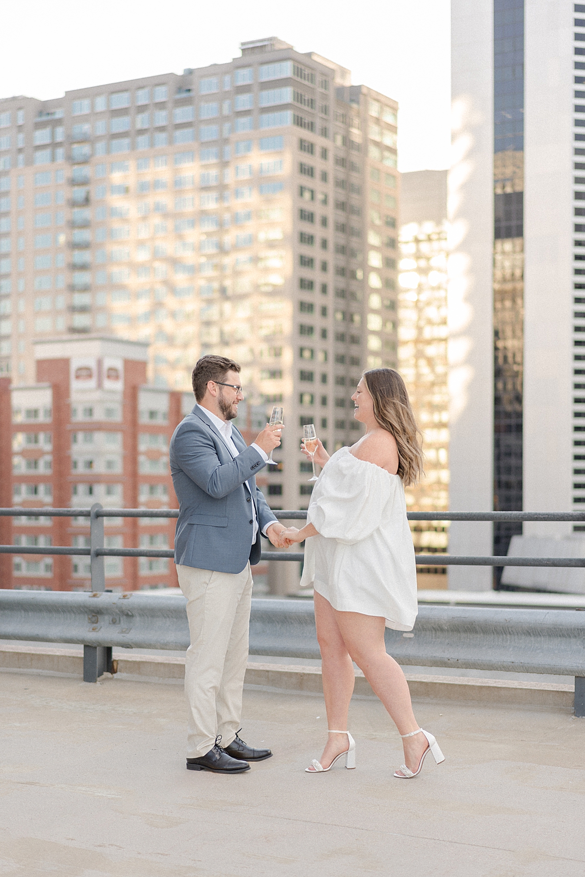 An engaged couple shares a glass of champagne on a rooftop with the Denver skyline