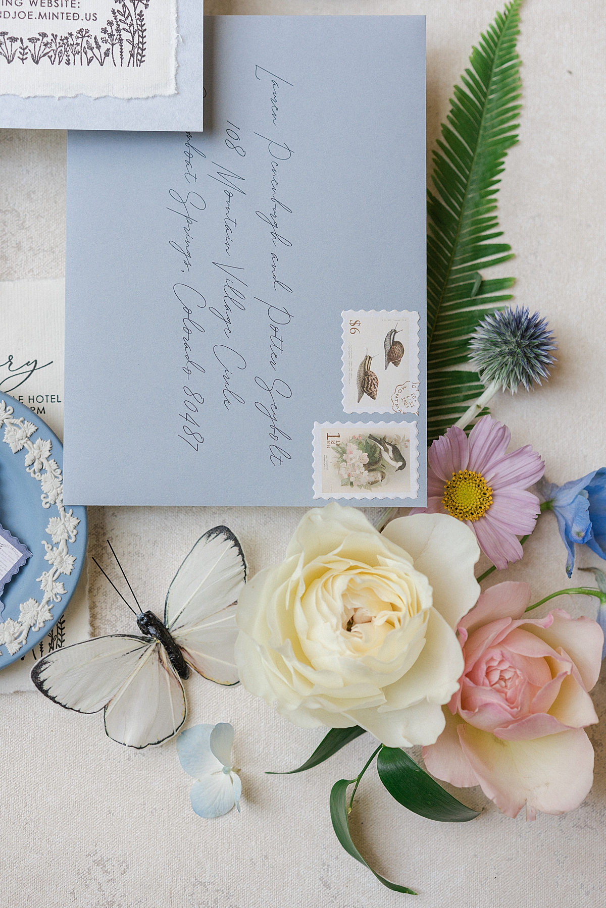 A beautiful flat lay with a blue envelope displays stamps with snails on them, stylized with pastel florals and a butterfly.