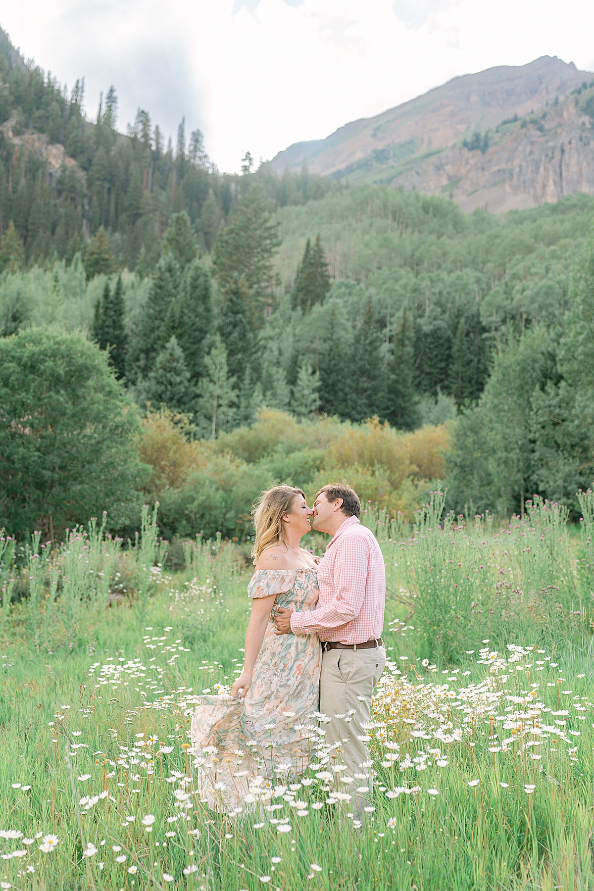 A couple kisses in the wild daisies in Aspen Colorado during their engagement photos.